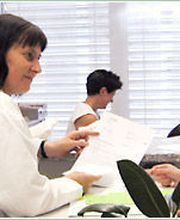 Ärztinnen besprechen Unterlagen am Empfangstresen, mit einer weiteren Frau im Hintergrund.