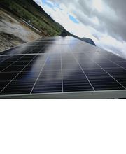 Paneles solares reflejando el cielo nublado, con montañas al fondo.