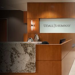 Wooden reception desk with "Udall Shumway" sign on wall and marble panel in modern office.