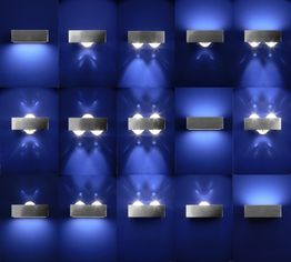 Mehrere silberne Wandleuchten auf blauer Wand in einem symmetrischen Muster angeordnet.