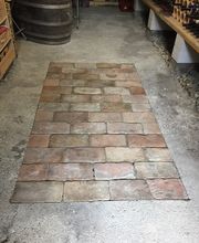 Backsteine im Boden eines Werkraums mit Holzregalen und einem Fass an den Seiten.