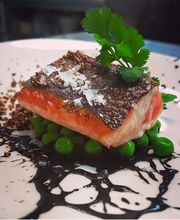 Salmon sobre guisantes con reducción oscura y hojas verdes decorativas.