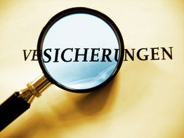 Lupe vergrößert das Wort "Versicherungen" auf einem Blatt Papier.