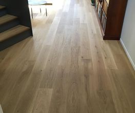 Helles Wohnzimmer mit Holzboden, Treppe links, Bücherregal rechts und Sofa im Hintergrund.