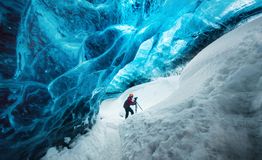 Pessoa caminhando em caverna de gelo azul com neve ao redor.