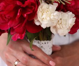 Mani di una sposa con anello tengono un bouquet di rose rosse e bianche.