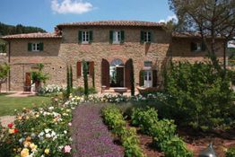 Casa di campagna in pietra con giardino fiorito e cielo sereno.