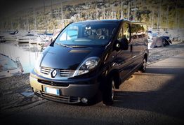 Furgone nero parcheggiato vicino a un porto con barche a vela sullo sfondo.