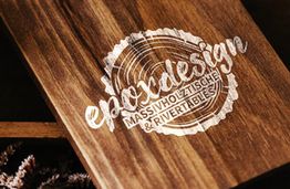 Holztafel mit dem Logo "epoxdesign", darunter "Massivholztische & Rivertables".