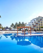 Hotel con piscina azul rodeada de palmeras, tumbonas y sombrillas bajo un cielo despejado.
