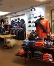 Modegeschäft mit Kleidung auf Tischen und Regalen, Schaufensterpuppen und helle Beleuchtung.