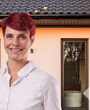 Drei Personen in weißen Hemden stehen vor einem modernen Haus mit Garten im Hintergrund.