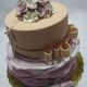 Torta a due piani decorata con fiori di zucchero rosa e crema su un vassoio dorato.