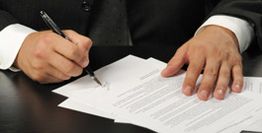 Person unterschreibt Dokumente am Schreibtisch.