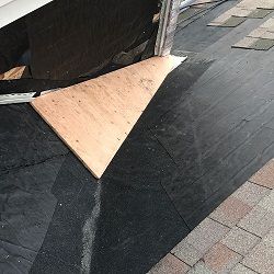 Roof repair with plywood and black waterproof material near shingles.
