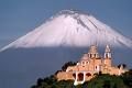 Vista del volcán nevado con una iglesia en primer plano sobre una colina verde.