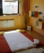 Ein einfaches Schlafzimmer mit Matratze am Boden und Fenster mit Blick auf Gebäude.