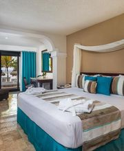 Habitación amplia con cama grande, decorada en tonos tierra y azul, vista al mar desde el balcón.