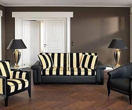 Wohnzimmer mit gestreiftem Sofa, zwei Sesseln, zwei Lampen und Holzboden. Wandfarbe ist braun.