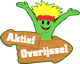Groene mascotte met rode hoofdband naast houten bord met tekst 'Aktief Overijssel'.
