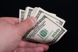 Hand holding a stack of hundred-dollar bills against a black background.