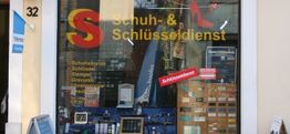 Schaufenster eines Schuh- und Schlüsseldienstes mit Angeboten für Schuhreparatur und Gravuren.