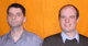 Zwei Männer stehen vor einem orangefarbenen Hintergrund, beide lächeln in die Kamera.