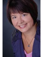 Frau mit braunen Haaren und lila Bluse lächelt in die Kamera.