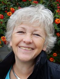 Een lachende vrouw met grijs haar voor een achtergrond van bloeiende oranje bloemen.