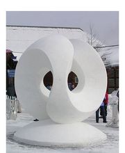 Eine große, abstrakte Schneeskulptur mit ineinandergreifenden Ringen auf einem schneebedeckten Platz.
