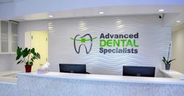 Dental office reception with a logo on a wavy wall and plants on the counter.