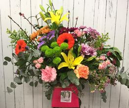 Ramo de flores variadas con lirios amarillos, gerberas naranjas y follaje verde. Fondo de madera.