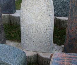 Einzigartig gestalteter, hellgrauer Grabstein mit radialem Muster, umgeben von anderen Steinen.
