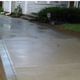 A wet concrete driveway next to a light-colored house and shrubs.