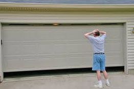 Person in shorts looks at a partially open garage door, appearing puzzled.