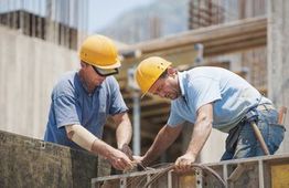 Two construction workers in hard hats secure wires at a building site.