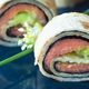 Lachs-Wraps mit Avocado und Nori auf blauem Teller, garniert mit Schnittlauchblüten.