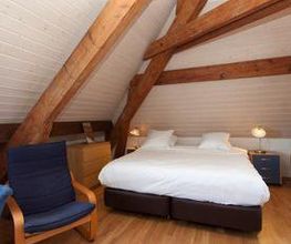 Dachgeschoss-Schlafzimmer mit Holzbalken, Doppelbett und Sessel auf Holzboden.