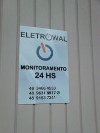 Placa da Eletrowal em parede, com contatos de monitoramento 24 horas e números de telefone.