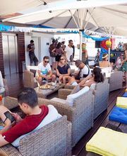 Grupo de personas relajadas en una terraza con sillones y sombrillas grandes.