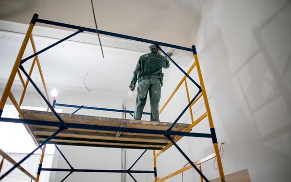Bauarbeiter steht auf Rollgerüst, um Putz an der Decke zu verputzen.