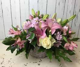 Arreglo floral con lirios rosados, rosas blancas y margaritas. Fondo de madera blanca.