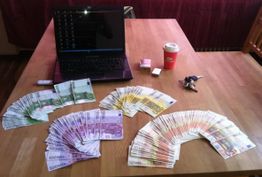 Ein Laptop, viel Bargeld, ein Kaffee, Schlüssel und USB-Stick auf einem Holztisch.