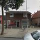 Een straatbeeld met een bakstenen gebouw, een fiets geparkeerd en enkele auto’s op de voorgrond.