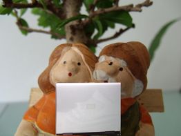 Tonfiguren-Paar mit Laptop, sitzt vor einem Baum. Beide schauen auf den Bildschirm.