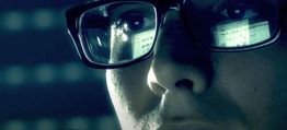 Nahaufnahme eines Gesichts mit Brille, in der sich ein Computerbildschirm spiegelt.