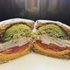 A sliced sandwich with turkey, cheese, tomato, lettuce, and avocado on whole-grain bread.