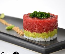 Tartar de atún, aguacate y arroz sobre plato negro, decorado con sésamo y wasabi.