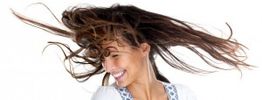 Frau lächelt mit im Wind wehenden Haaren vor weißem Hintergrund.