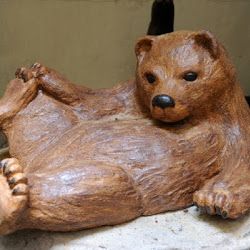 Braunbär-Statue liegt entspannt auf dem Rücken mit Pfoten angehoben, auf einem Sockel.